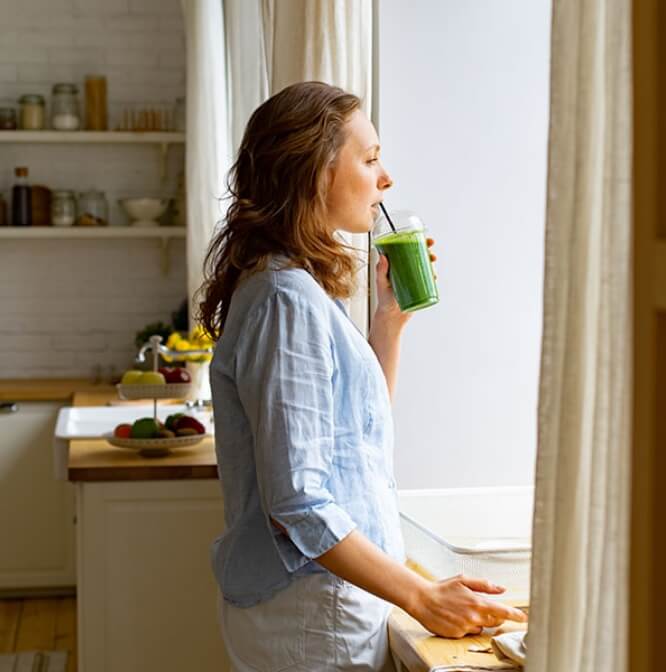 Woman looking out window drinking a green shake